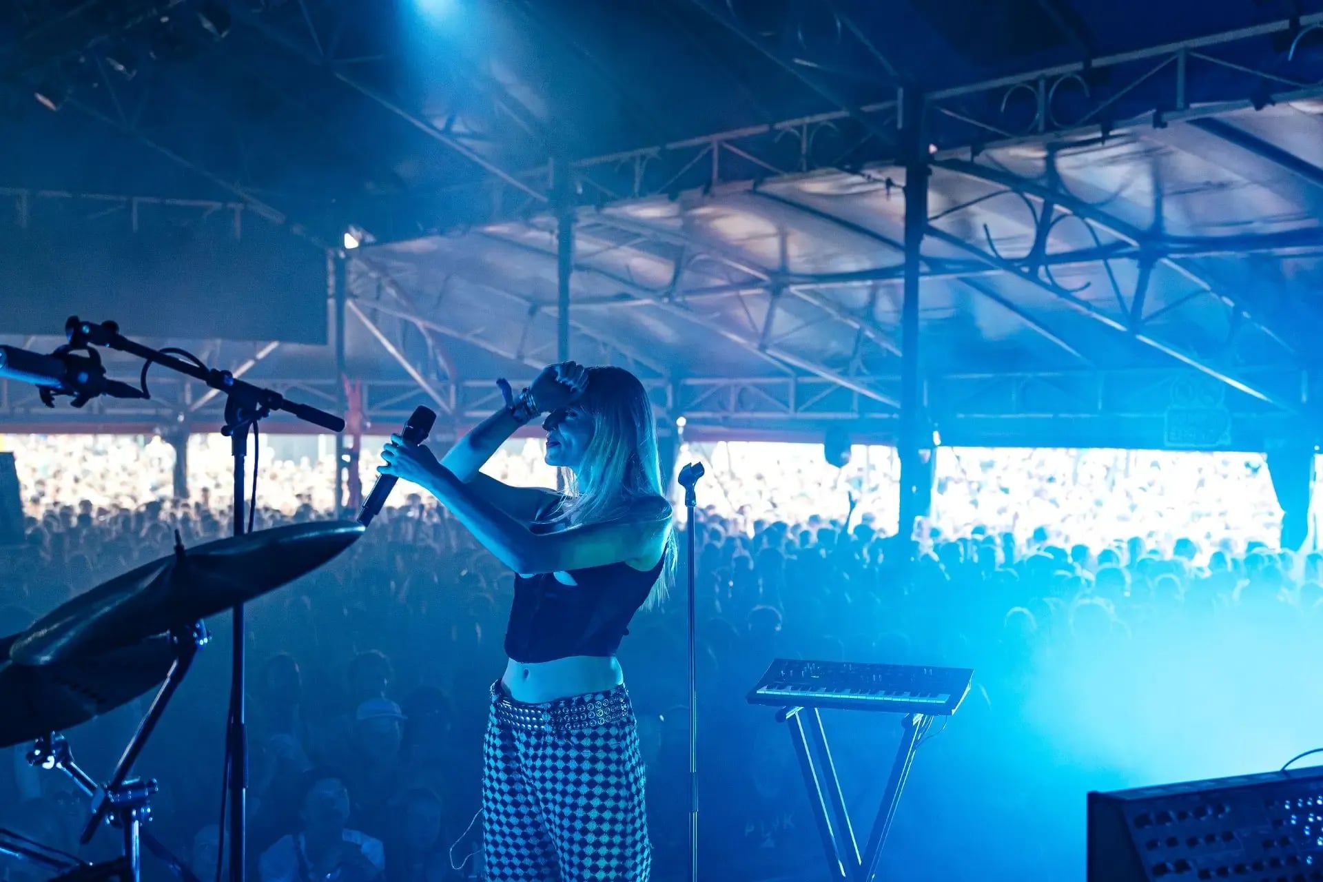 Zangeres staat op een podium met op de achtergrond publiek. Ze heeft een microfoon in haar ene hand. De andere hand ligt op haar voorhoofd.