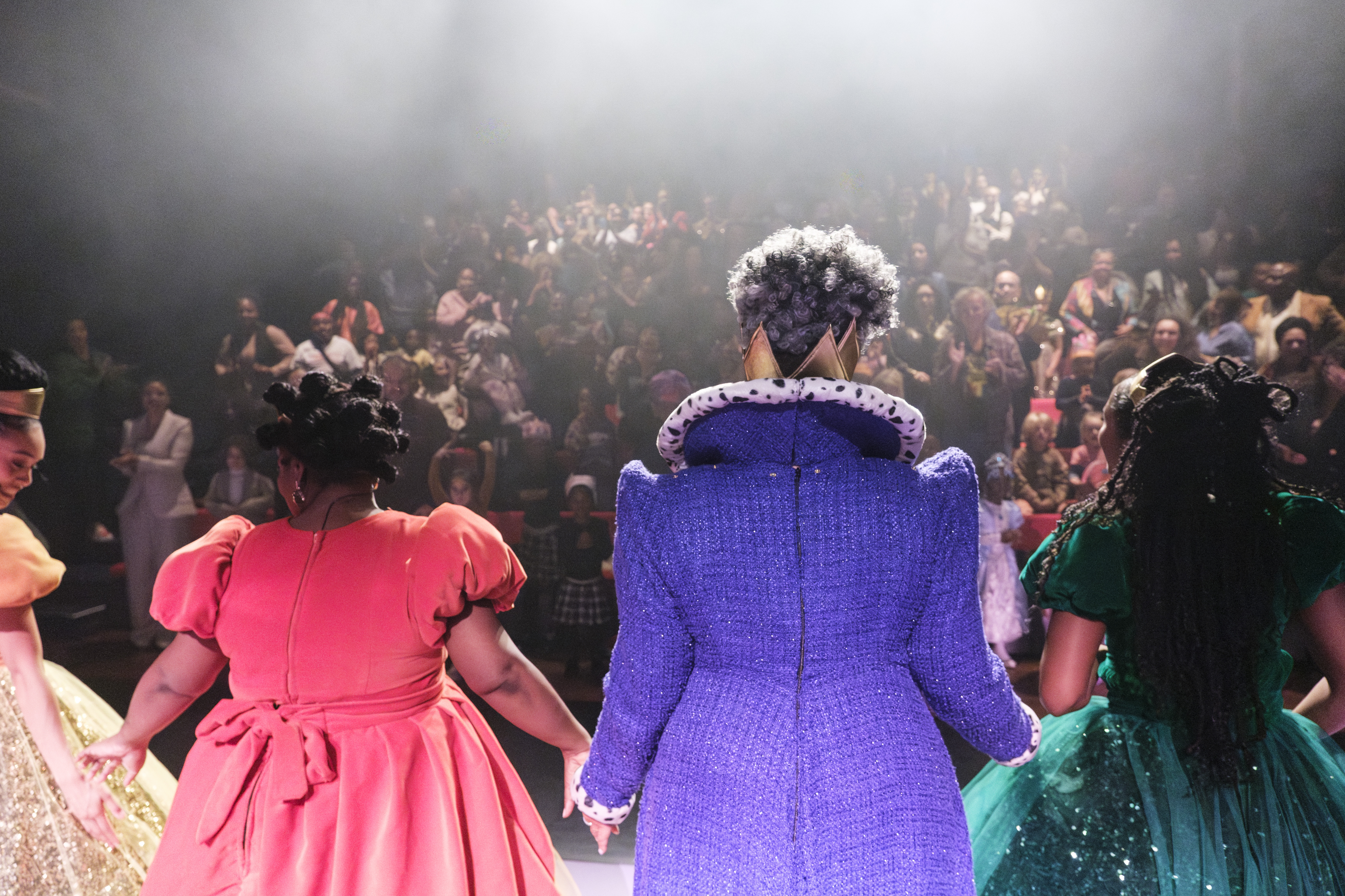Acteurs in kleurrijke kostuums staan hand in hand op een podium en buigen naar het publiek.