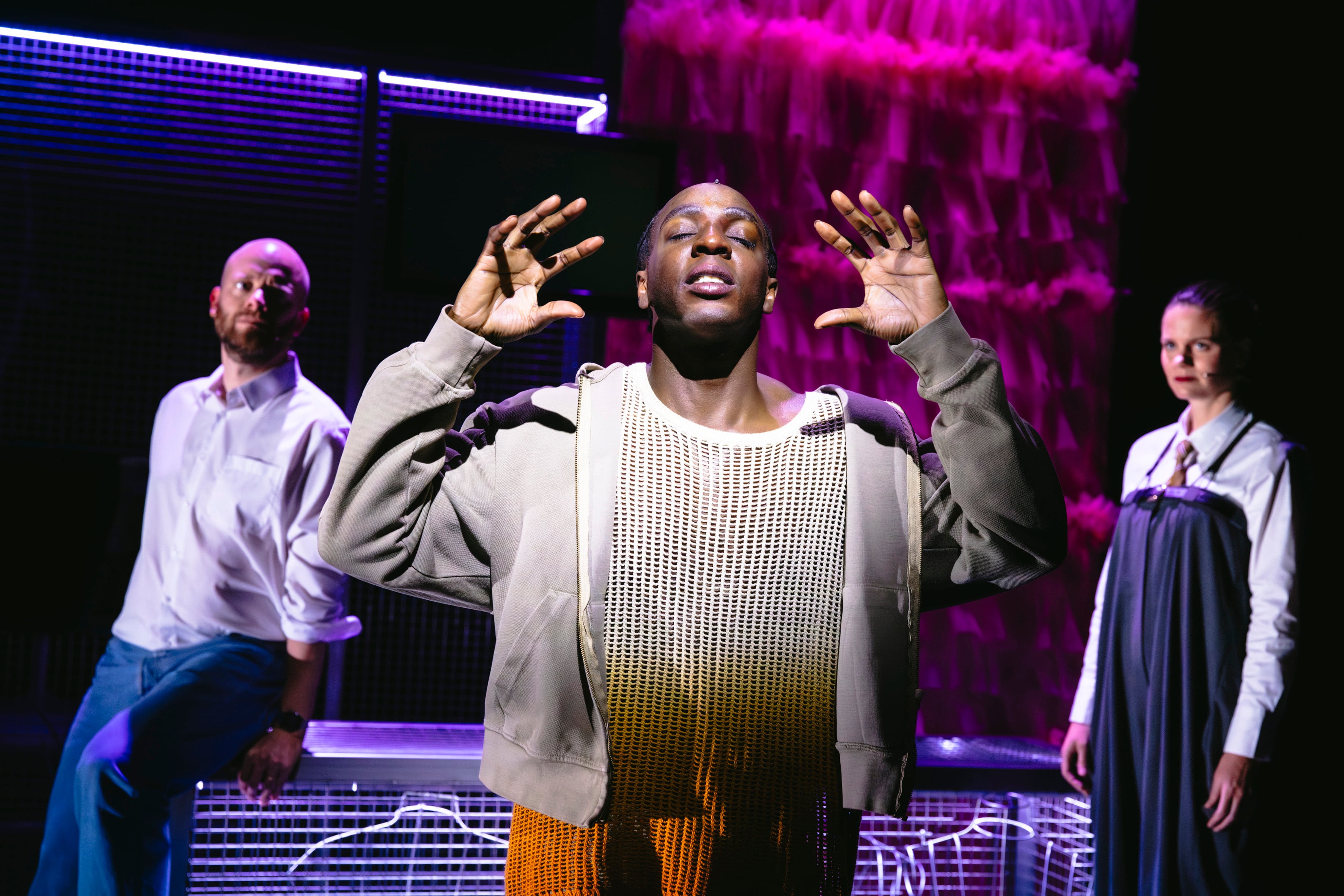 Drie acteurs staan op het podium, de middelste heeft zijn ogen gesloten en houdt zijn handen omhoog als in concentratie