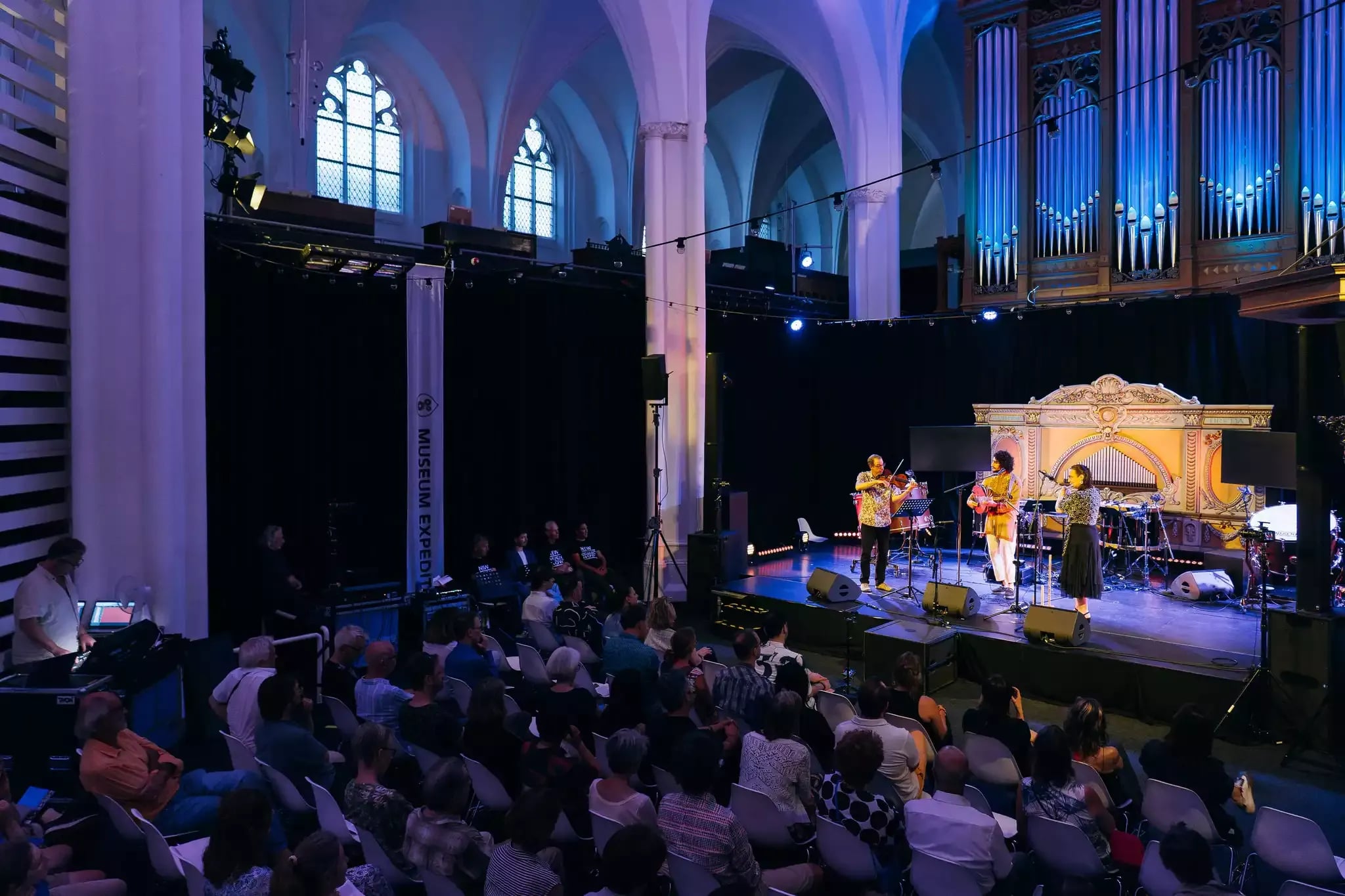 Publiek kijkt naar Nawras Altaky (ud, zang), Marianne Noordink (ney) en Oene van Geel (altviool) in Museum Speelklok, Utrecht. Foto: Almicheal Fraay. 