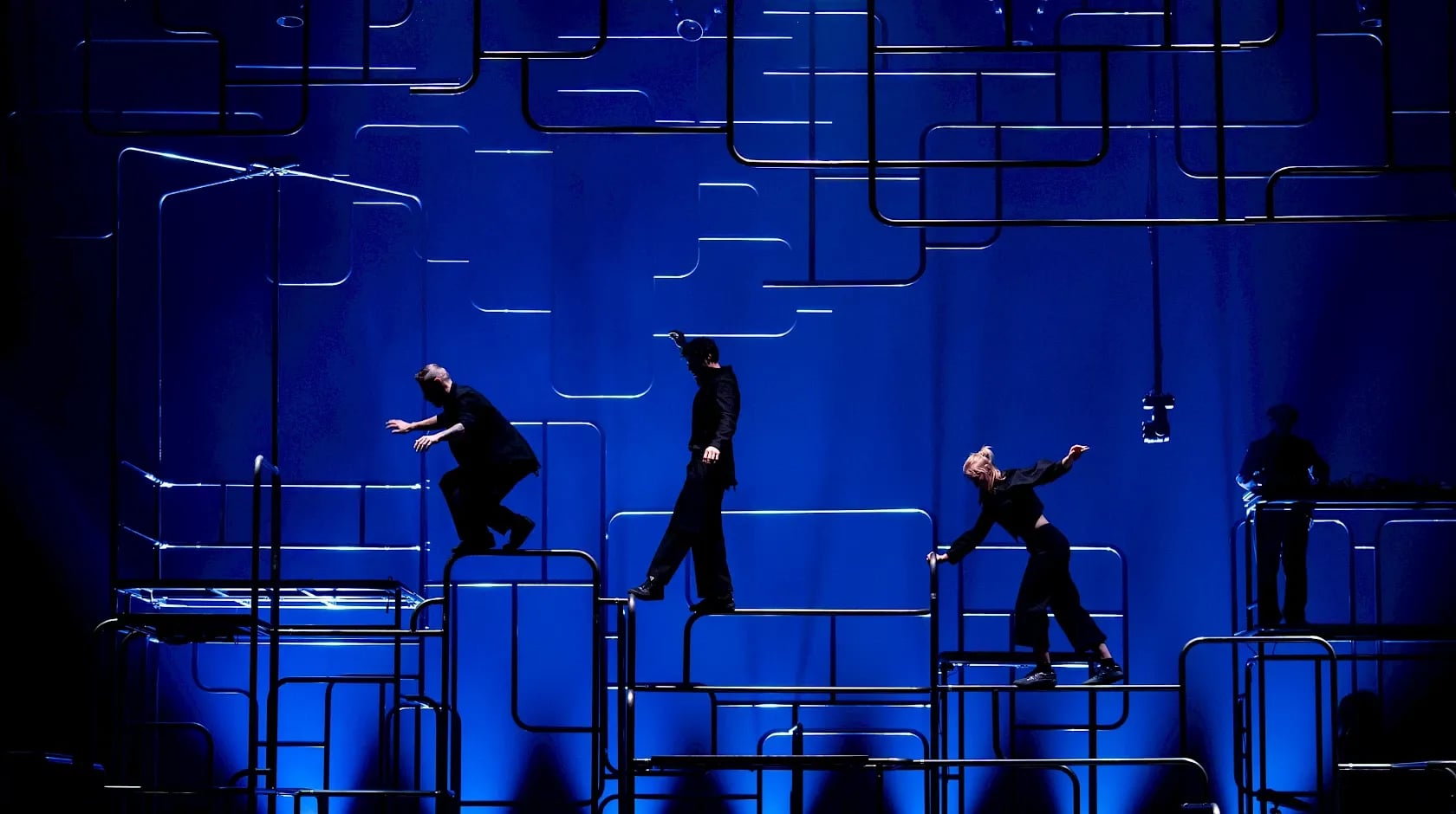 Drie dansers lopen over staven. De achtergrond heeft een spannende donkerblauwe kleur.