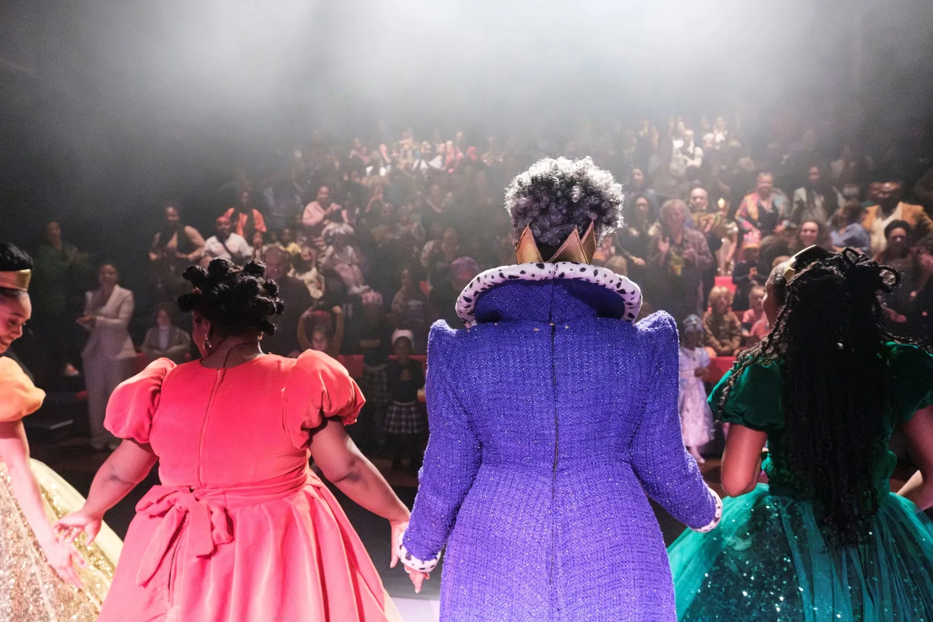 Castleden in kleurrijke kostuums staan hand in hand op een toneel en nemen een buiging voor een volle theaterzaal